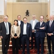 Gruppe von sieben Personen in formeller Kleidung vor einer Treppe.