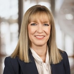 Lächelnde Frau in einem Anzug vor verschwommenem Hintergrund.