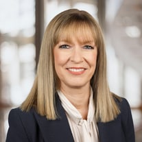 Lächelnde Frau in einem Anzug vor verschwommenem Hintergrund.