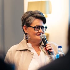 Person mit Brille spricht in Mikrofon bei Veranstaltung.