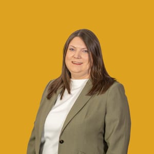 Frau in grüner Jacke vor gelbem Hintergrund.