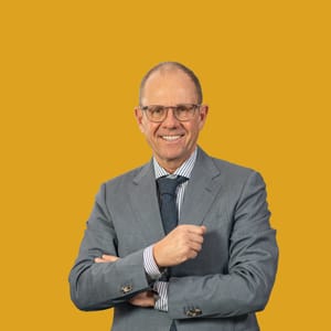 Mann im Anzug vor gelbem Hintergrund lächelt in die Kamera.