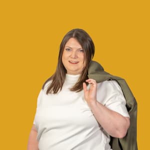 Frau vor gelbem Hintergrund mit Jacke über Schulter.