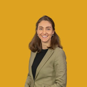 Frau in beigem Blazer vor gelbem Hintergrund lächelnd.