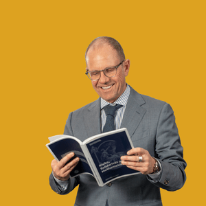 Mann in Anzug liest Buch vor gelbem Hintergrund.