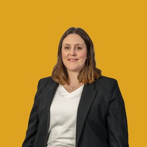 Frau in schwarzem Blazer vor gelbem Hintergrund.