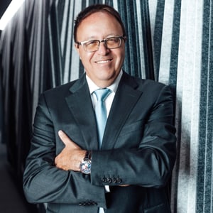 Mann im Anzug steht lächelnd vor gestreifter Wand.