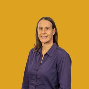 Frau vor senfgelbem Hintergrund, in lila Bluse.