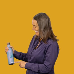 Frau zeigt auf eine Wasserflasche vor gelbem Hintergrund.