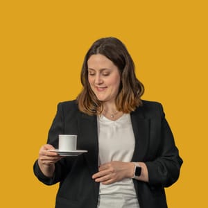 Frau hält eine Tasse vor gelbem Hintergrund.