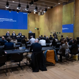 Konferenzraum mit Rednern und Publikum auf Stühlen.