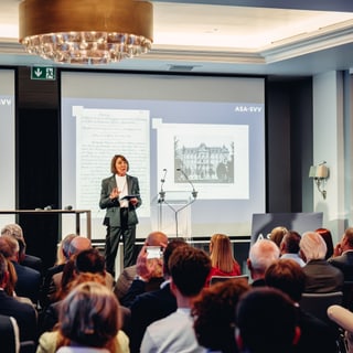 Konferenzredner auf der Bühne mit Publikum im Konferenzraum.