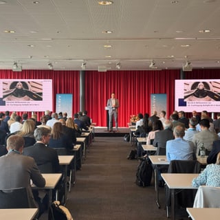 Konferenzraum mit vielen Menschen und einer Person auf der Bühne.