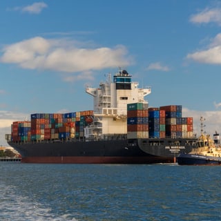 Containerschiff im Hafen mit Frachtcontainern und Schlepperboot.