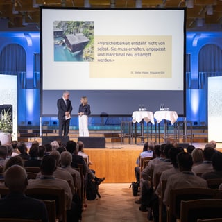 Menschen sitzen in einem Auditorium und schauen zu einer Präsentation auf der Bühne.
