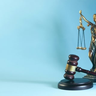Justitia-Statue mit Waage und Richterhammer vor blauem Hintergrund.