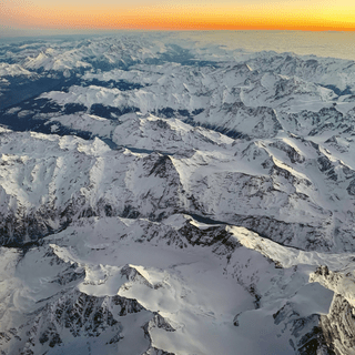 Luftaufnahme von verschneiten Bergen bei Sonnenuntergang.