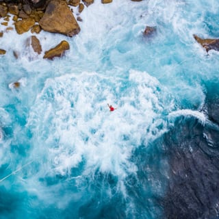 Luftbild einer Person in rauer Brandung neben Felsen.