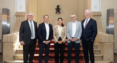 Fünf Personen in formeller Kleidung stehen vor einer Treppe.