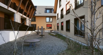 Spielplatz zwischen zwei Gebäuden mit Kiesboden.