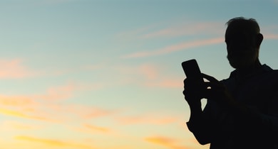 älterer Mann mit Handy in der Dämmerung