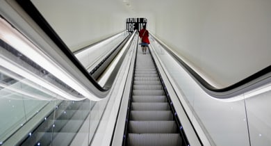Person auf Rolltreppe nach oben in modernem Gebäude.