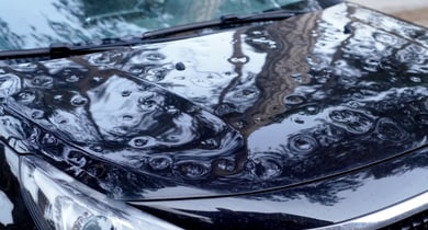 Nahaufnahme der Dellen auf einer schwarzen Motorhaube eines Autos.