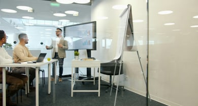Person steht vor einem Bildschirm und präsentiert in einem Büro.