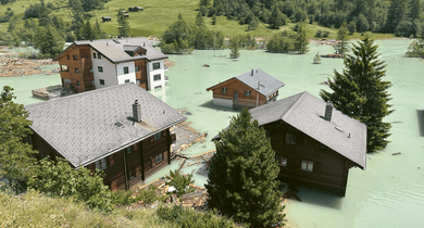Überflutete Holzhäuser in einer grünen Berglandschaft.