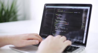 Hände tippen auf einem Laptop mit Code auf dem Bildschirm.