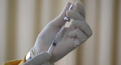 Person mit Handschuhen zieht Flüssigkeit in Spritze auf.