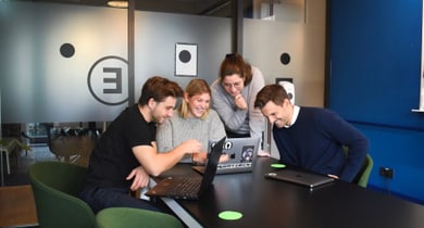 Vier Personen an einem Tisch, die auf einen Laptop schauen und lächeln.