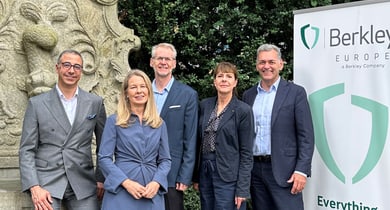 Fünf Personen in Geschäftskleidung neben einem Steindenkmal und einem Berkley Europe Banner.