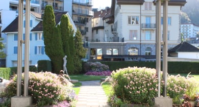 Garten mit Blumen und Statuen vor Gebäuden.