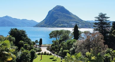 Blick auf See und Berge mit Bäumen im Vordergrund.