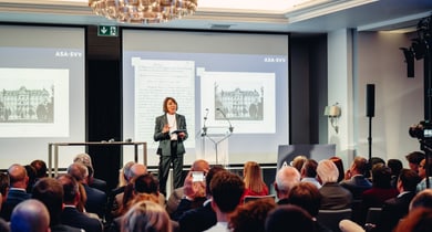 Konferenzredner auf der Bühne mit Publikum im Konferenzraum.