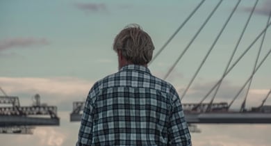 Person mit kariertem Hemd steht vor einer Brücke.