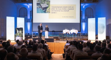 Menschen sitzen in einem Auditorium und schauen zu einer Präsentation auf der Bühne.