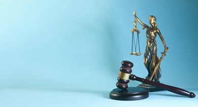 Justitia-Statue mit Waage und Richterhammer vor blauem Hintergrund.