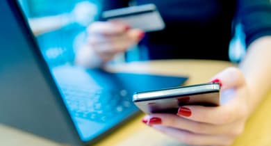 Frau mit Handy und Kreditkarte am Laptop