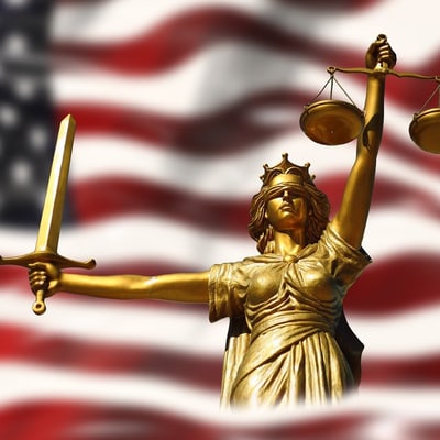 Die amerikanische Flagge mit der Figur der Justita, stellvertretend für US-Risiken, über die Referierende an der Fachtagung sprechen werden