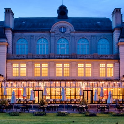 Beleuchtetes Gebäude bei Dämmerung mit Garten im Vordergrund.