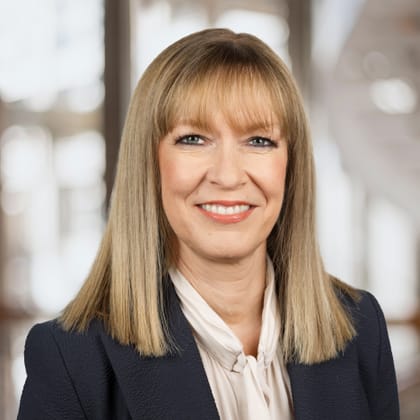 Lächelnde Frau in einem Anzug vor verschwommenem Hintergrund.