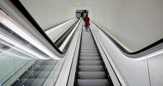 Person auf Rolltreppe nach oben in modernem Gebäude.
