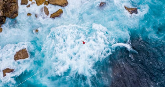 Luftbild einer Person in rauer Brandung neben Felsen.