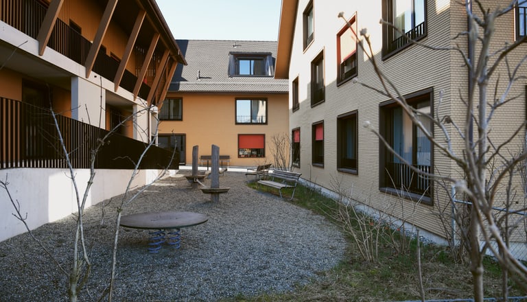 Spielplatz zwischen zwei Gebäuden mit Kiesboden.