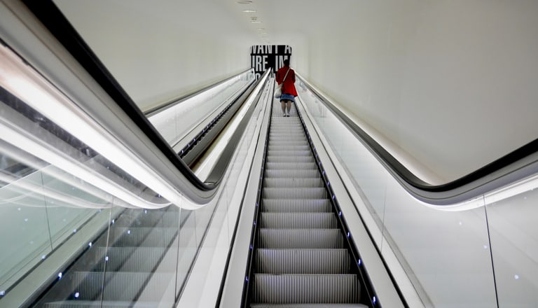 Person auf Rolltreppe nach oben in modernem Gebäude.
