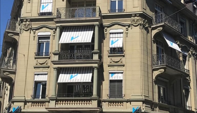 Historisches Gebäude mit Markisen und blauen Logos auf Fassade.
