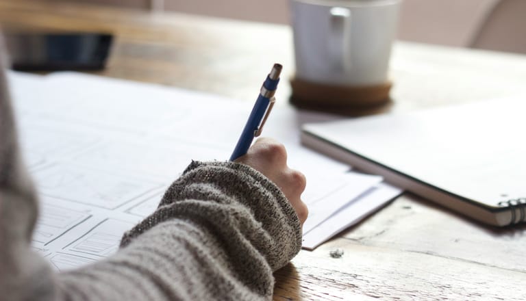 Hand schreibt mit einem Stift auf Papier.