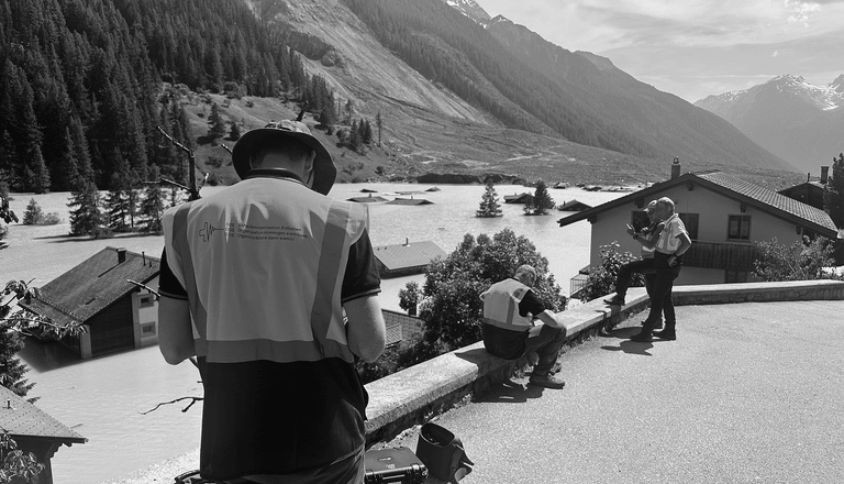 Drei Personen bei der Arbeit in bergiger Landschaft mit Häusern.